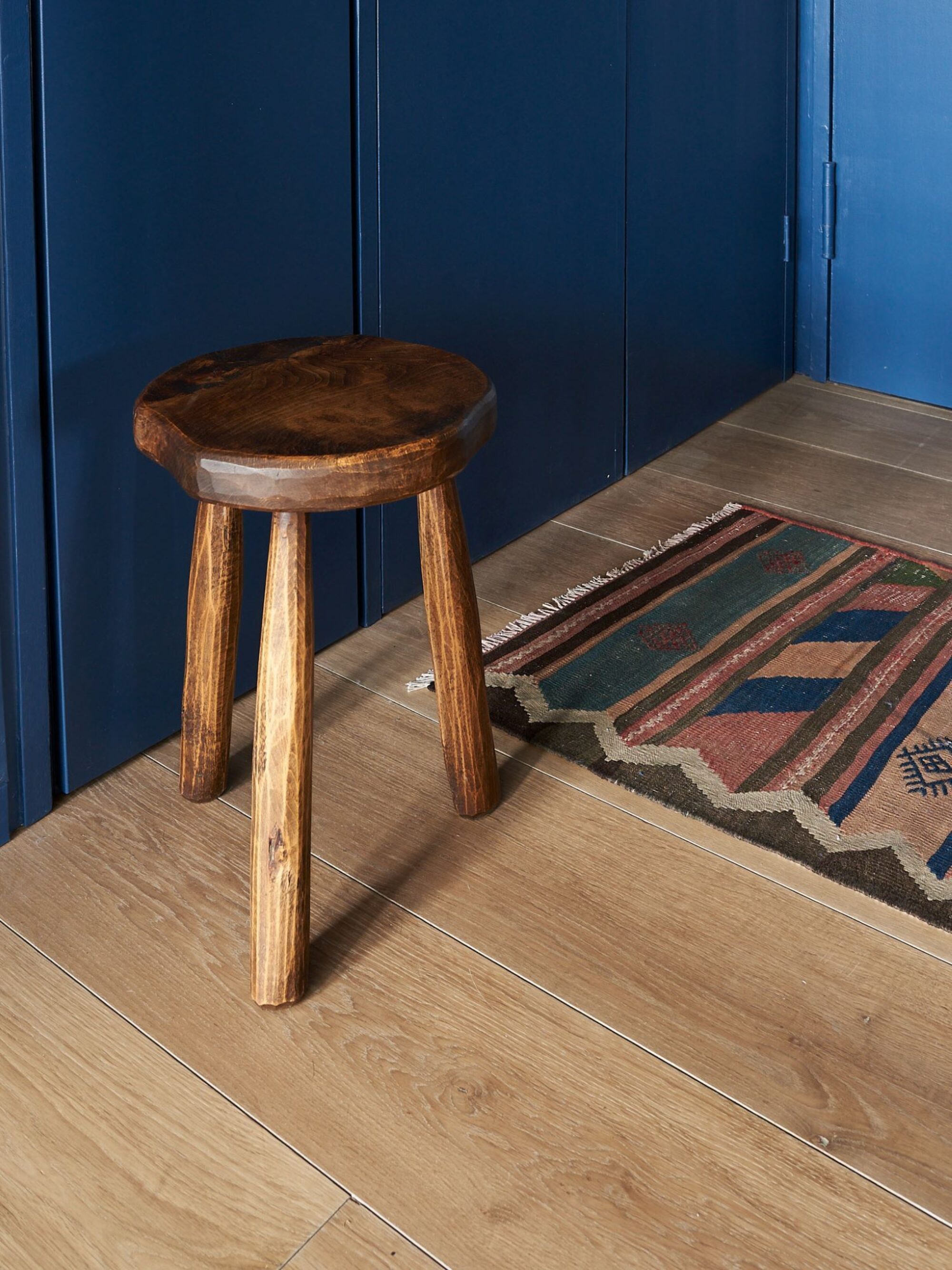 Top down image showing a light oak floor with a vintage stool, Kelim rug and Prusian blue walls.