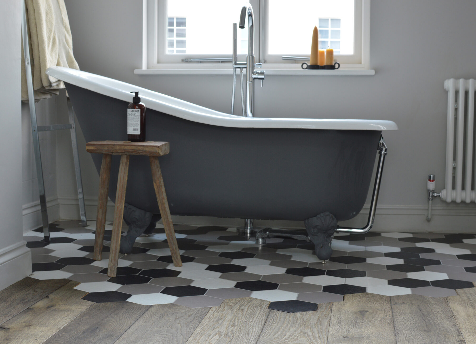 Oak magma stromboli plank meeting hexagon tiles with a free standing bath and wooden stool