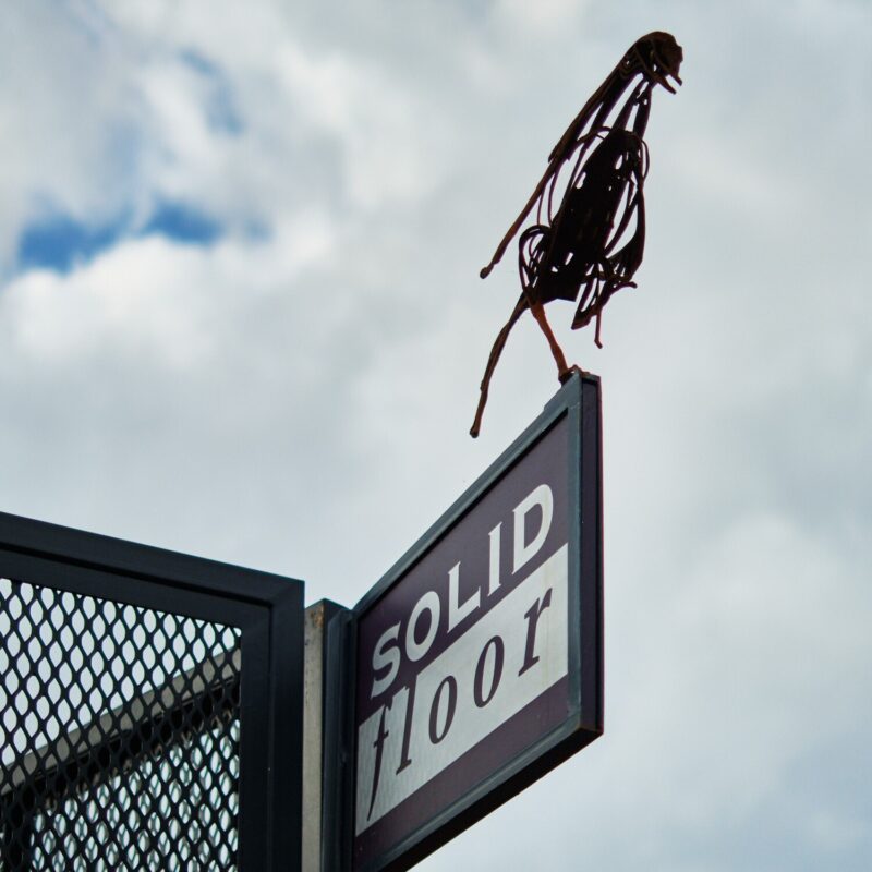 Solid floor sign on fence with bird sculpture